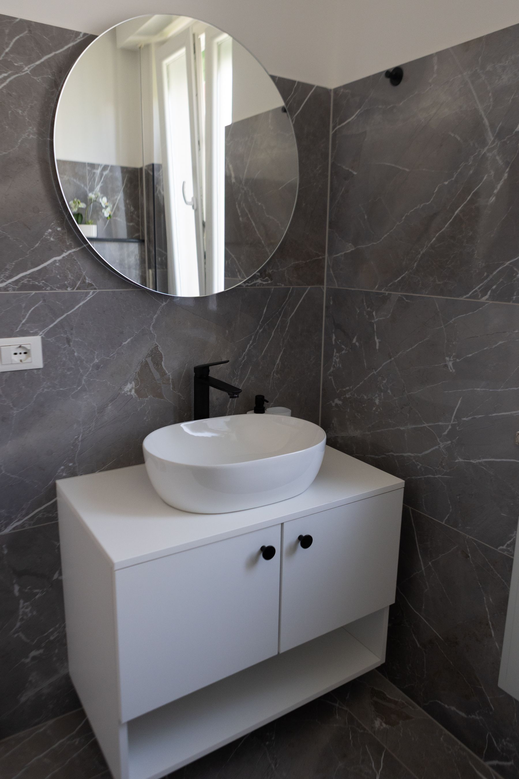 Lavabo in ceramica bianca e specchio tondo su parete in marmo grigio