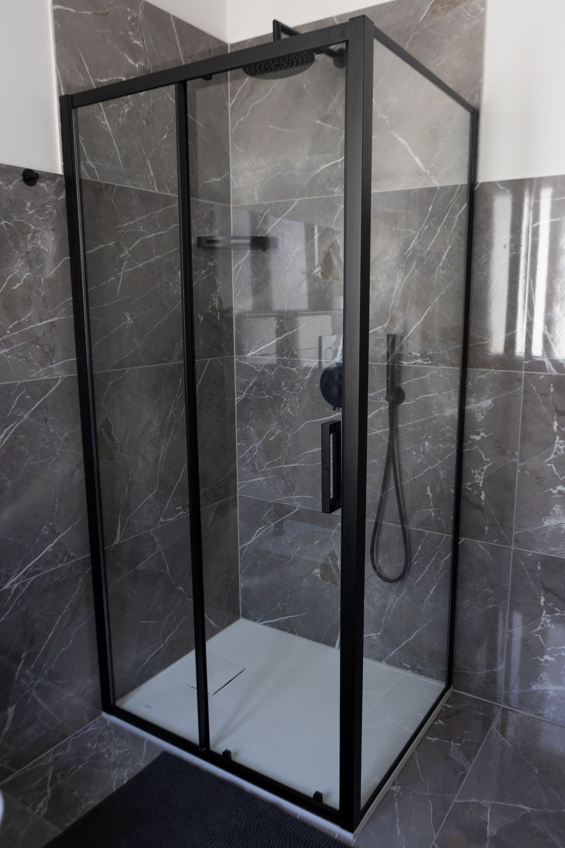 Doccia con box in vetro e profili neri, rivestimento in marmo grigio