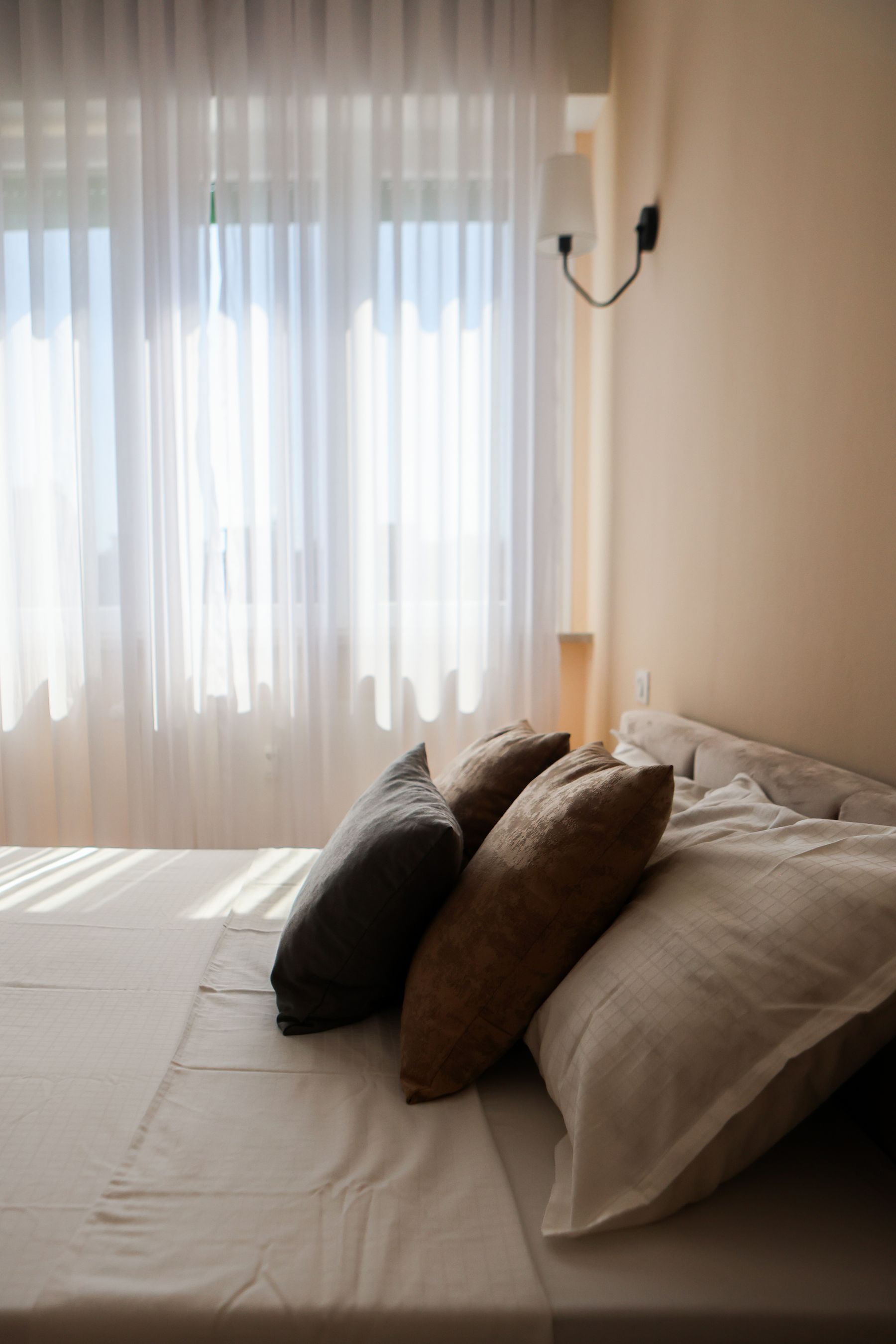 Luce del sole che filtra attraverso una tenda leggera su un letto con cuscini in lino