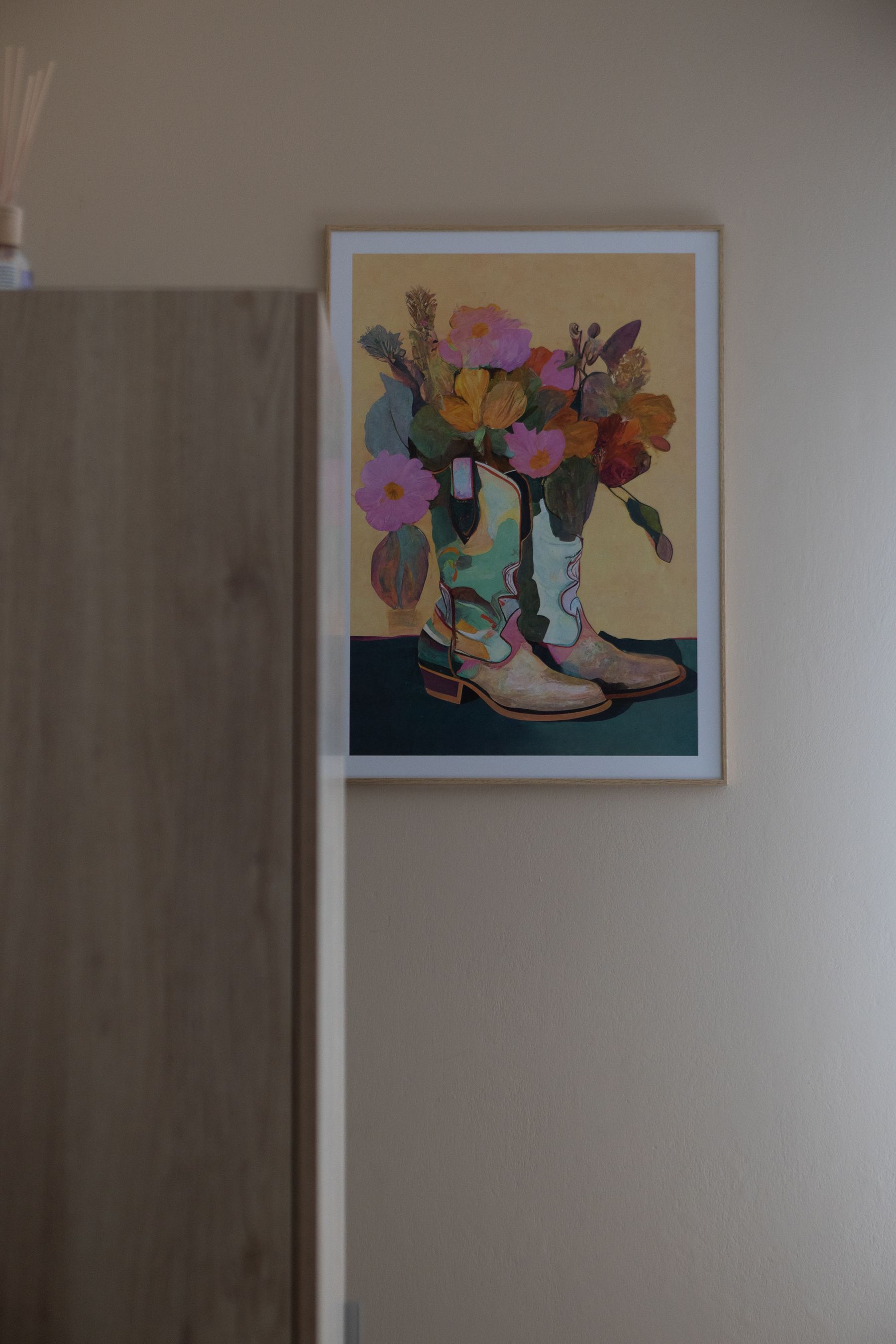 Stampa colorata con un vaso di fiori accanto a un armadio in legno chiaro