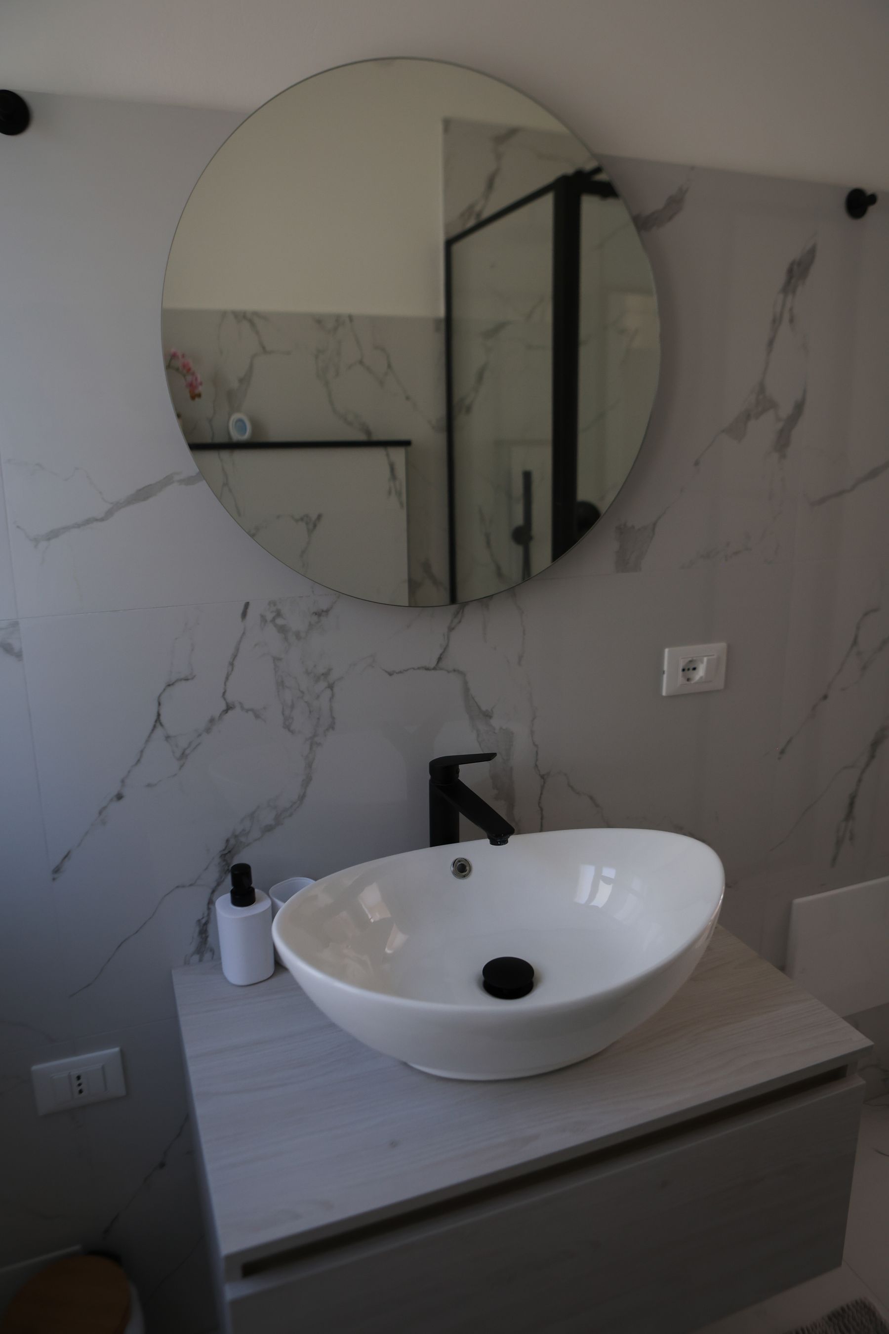 Lavabo da appoggio bianco e specchio rotondo su parete in marmo bianco