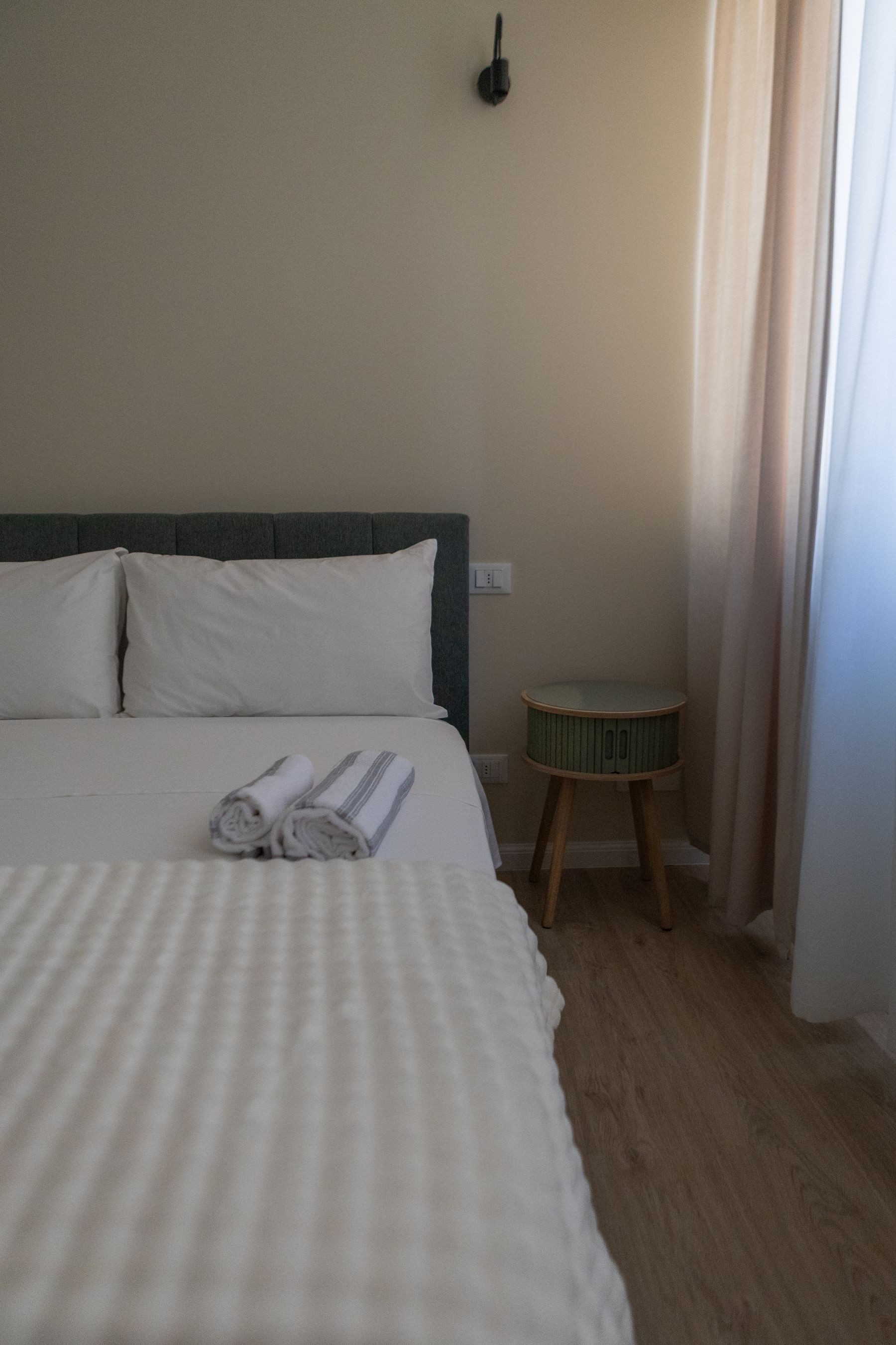 Letto con testiera verde, comodino tondo in legno e luce naturale