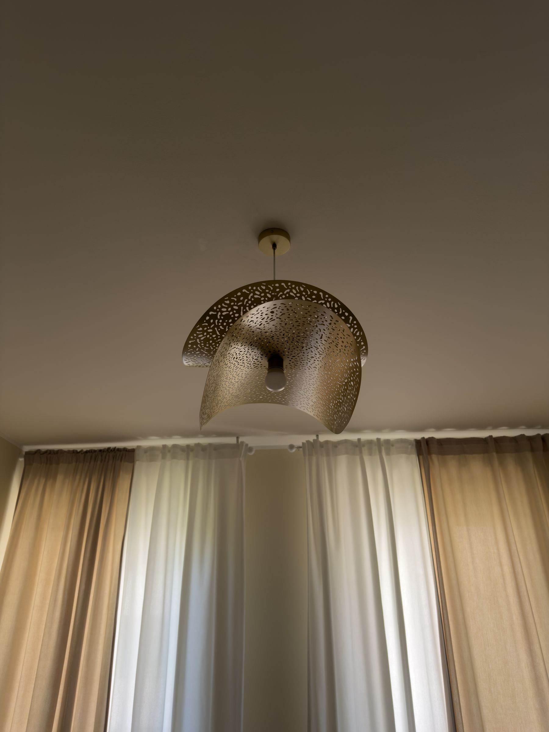 Lampada a sospensione in ottone traforato che diffonde una luce calda